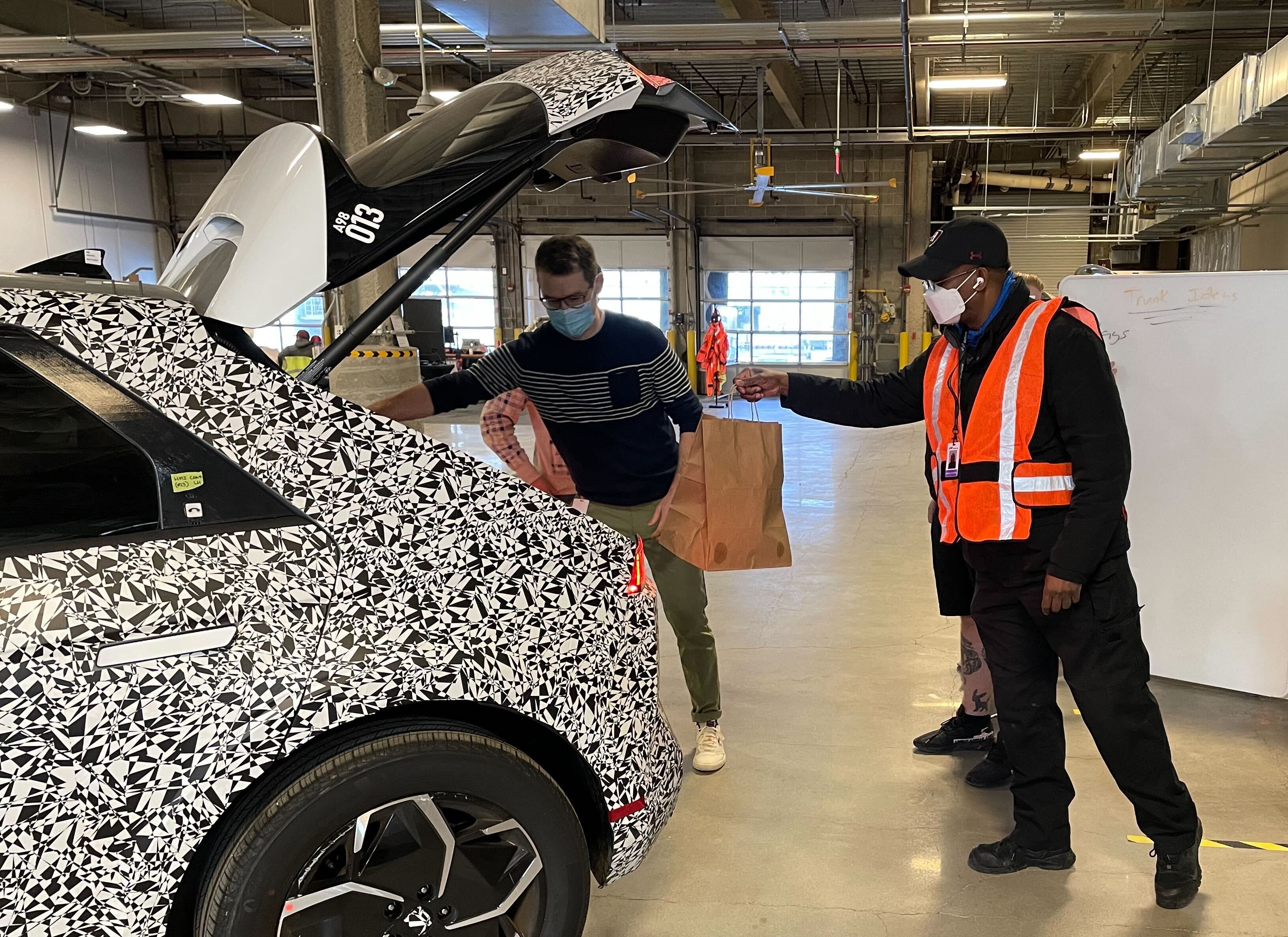 Motional employees stand at the rear of an IONIQ 5 robotaxi placing bags in the trunk