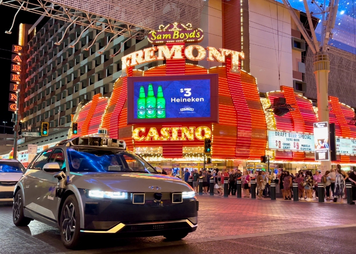 A gray IONIQ 5 robotaxi drives down Fremont Street in Las Vegas. A brightly lit casino is in the background. 