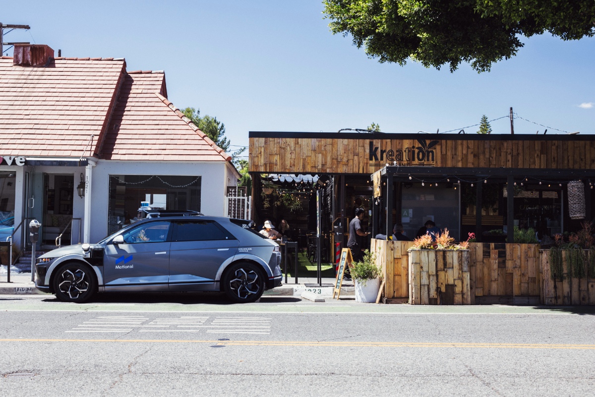 A gray IONIQ 5 robotaxi is parked at a commercial curbside in front of a restaurant in Santa Monica