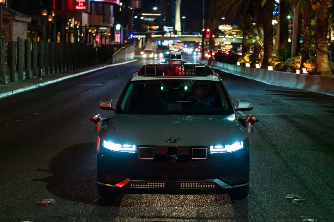A silver Motional IONIQ 5 robotaxi drives at nighttime along the Las Vegas Strip, its LED headlights shining