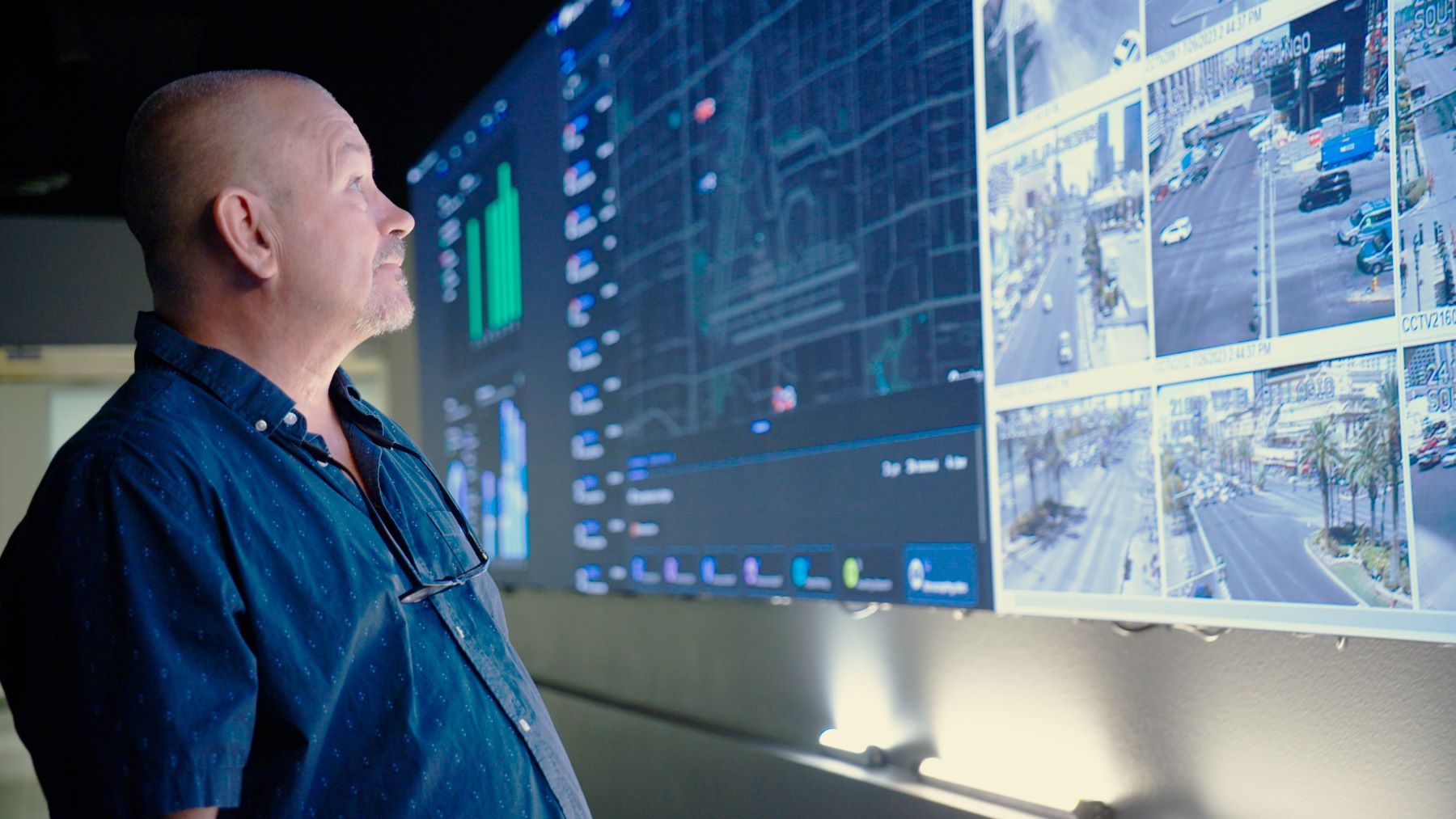 A man stands in front of a large screen looking at traffic cameras showing intersections around a city.